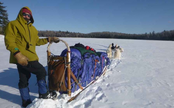 a gap year student poses with a dog sled in on a frozen, snowy lake lined with trees
